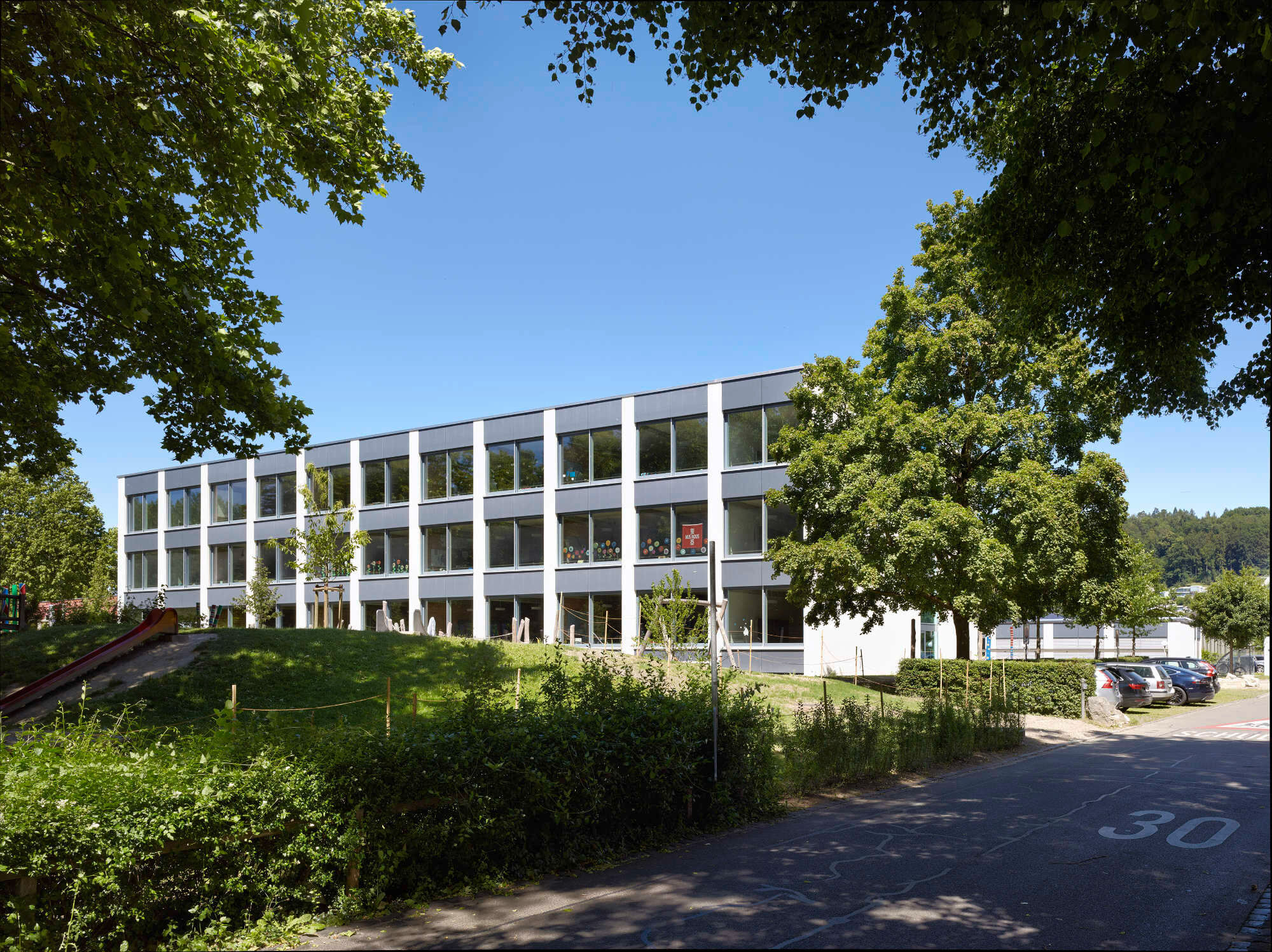 Stützen, Fensterfelder und dunkle Brüstungselemente gliedern den verlängerten Baukörper in gleichmäßigem Takt.