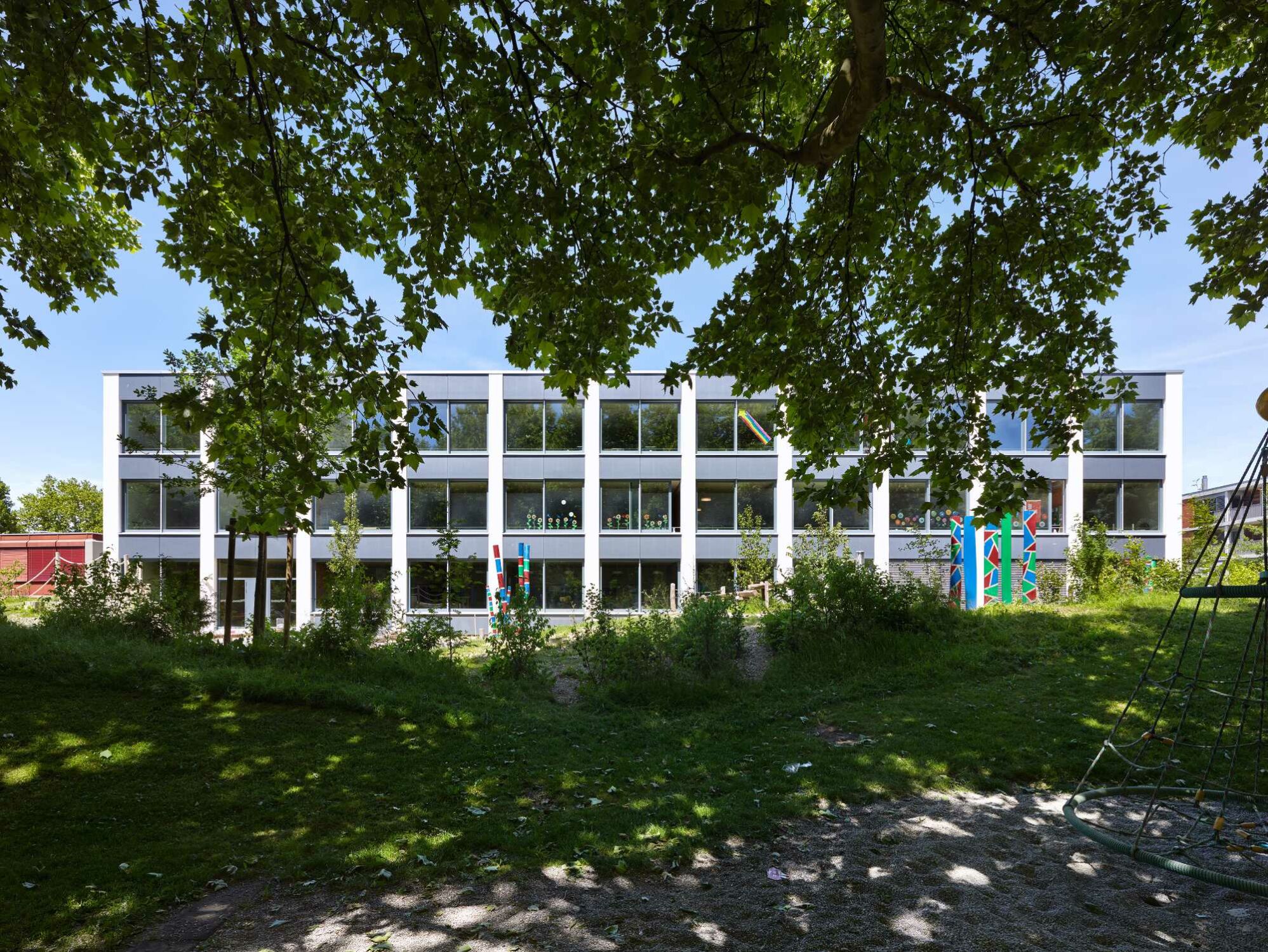 Auf der Südseite öffnet sich das Schulhaus zum begrünten Außenraum und zum neu gestalteten Spielbereich.