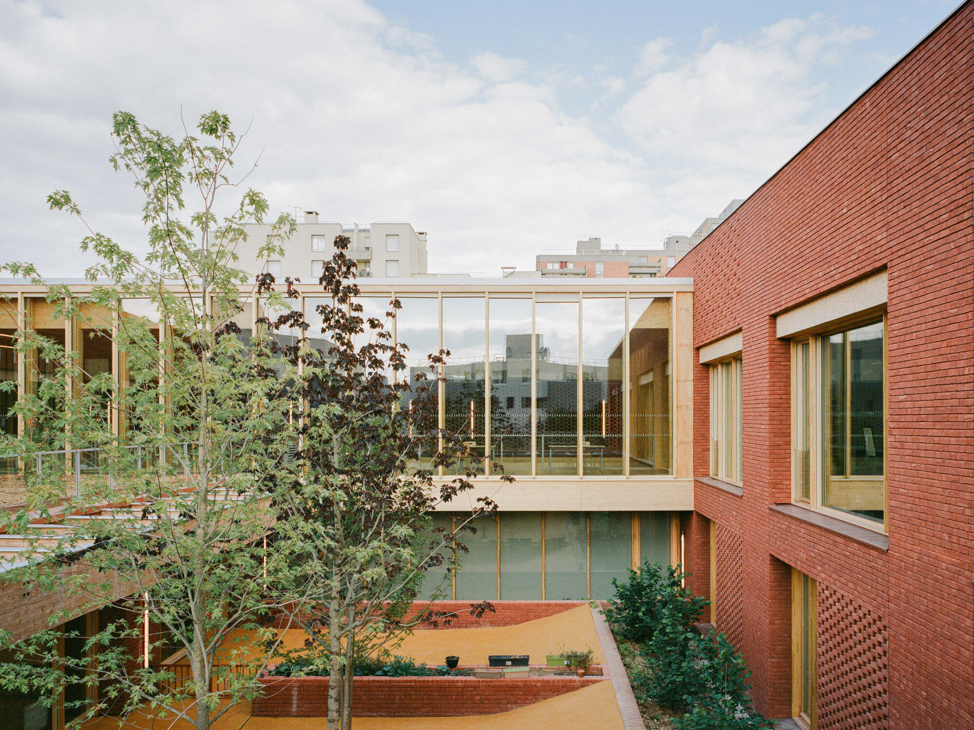 Blick auf den Haupteingang des von HEMAA Architectes geplanten, mehrgliedrigen Gebäudekomplexes gegenüber eines öffentlichen Platzes.