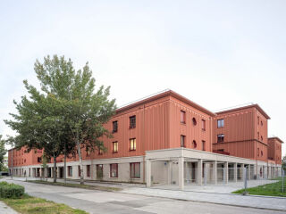 Das Erdgeschoss ist als robuster Sockel aus Betonfertigteilen ausgebildet; die Fassade darüber besteht aus vorgefertigten Holzrahmenelementen.