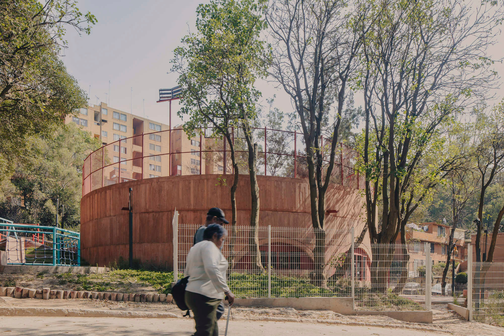 Von der Straße erscheint der pigmentierte Betonbau als geschlossener Zylinder zwischen altem Baumbestand und Wohnhäusern.