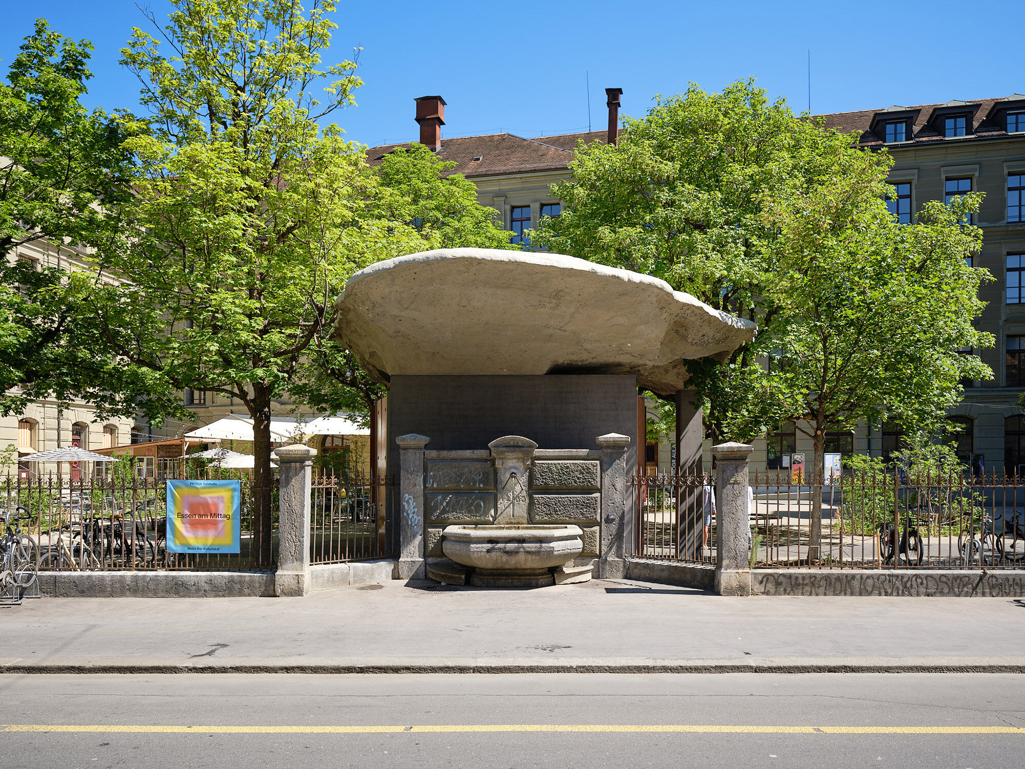 Eine kniehohe Mauer mit Zaun trennt den Hof vom Straßenraum, doch führen Tore in den Hof. Mittig befindet sich ein Trinkbrunnen, der zu einem wichtigen Ankerpunkt der Neugestaltung wurde.