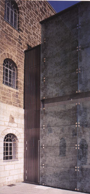Renovierte Sandsteinmauern spiegeln sich in bedruckten Glaspaneelen der neuen Rückfassade.
