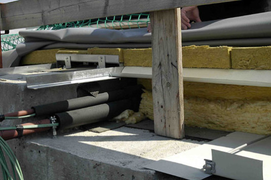 Dachschichten im Einzelnen: Betontragschale mit Überzug (links) und haustechnischen Leitungen; bituminöse Dampfsperre; Dämmschicht; Winkelprofil am Überzug als Auflage für Trapezblechschalung; Dämmschicht und Tragelemente für die Teller auf dem Überzug; Abdichtung aus Kunststoff
