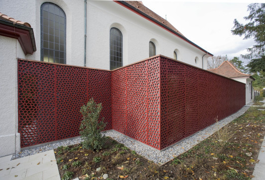Rote, amorph perforierte Fassadenplatten bedecken den Anbau vollflächig