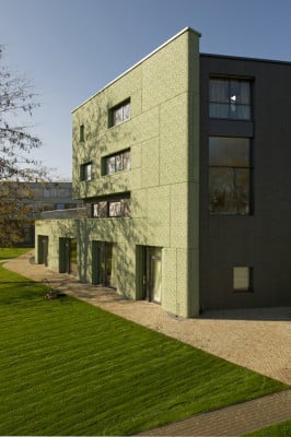 Hinter einer grünen Betonwand liegt der mit Naturstein verkleidete Baukörper des Konsulates