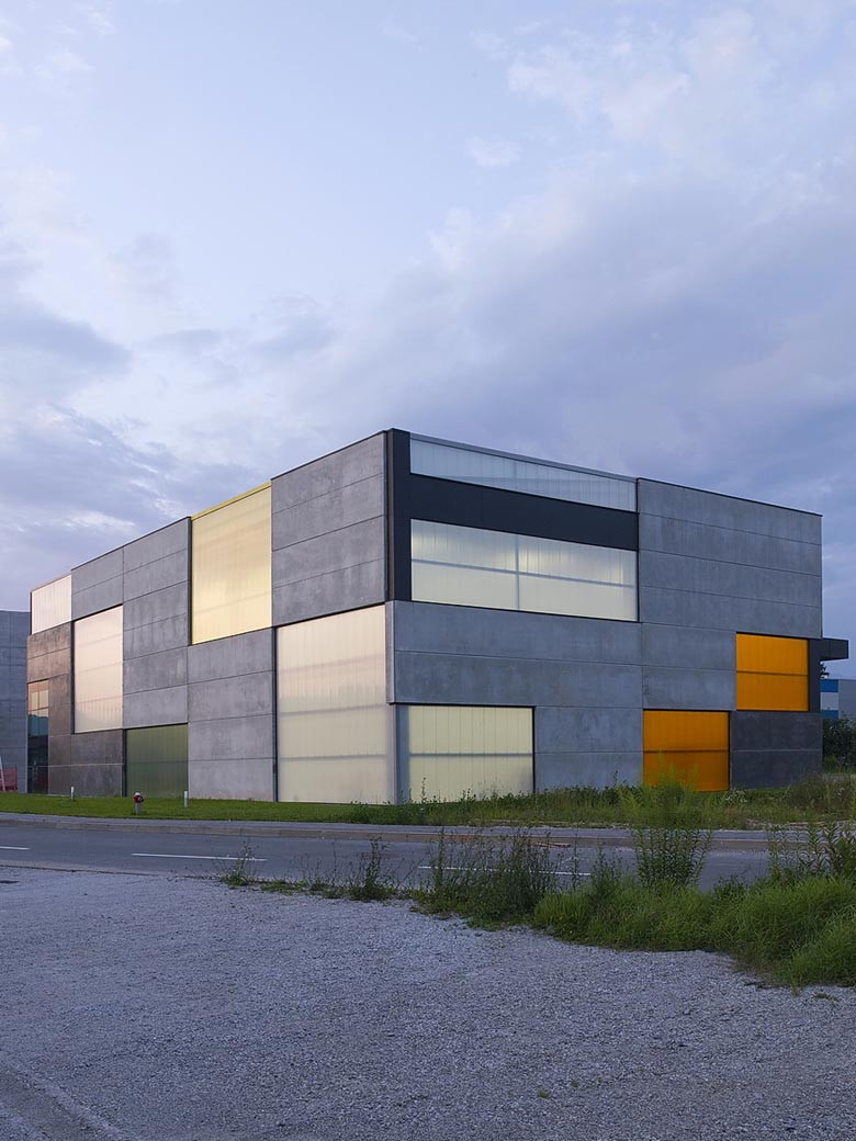 Fassade aus Betonfertigteilen, transluzenten Polycarbonatpaneelen und farbigen Metalltoren mit dunklen Vordächern