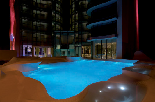 Geschwungener, weißer Pool vor dem Eingangsbereich am Abend